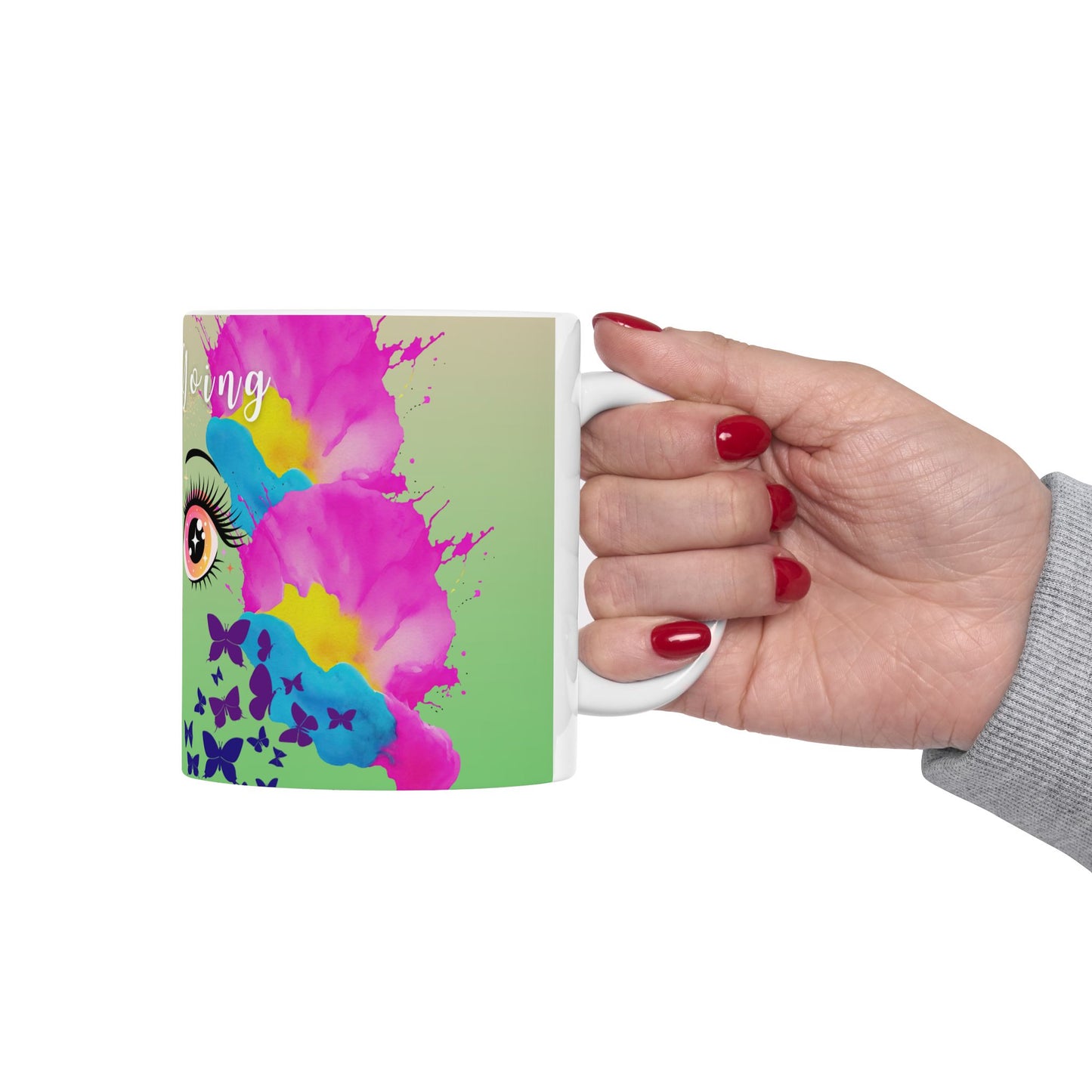 Hand holding a colorful mug with a design of an eye, butterflies, and abstract patterns on a white background.